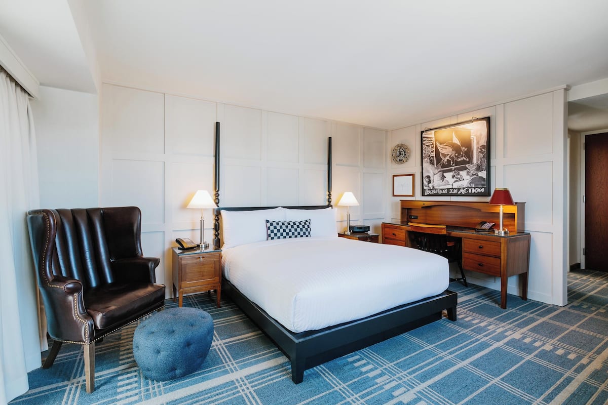A hotel room with a large bed, a leather armchair, a desk, and a blue patterned carpet.