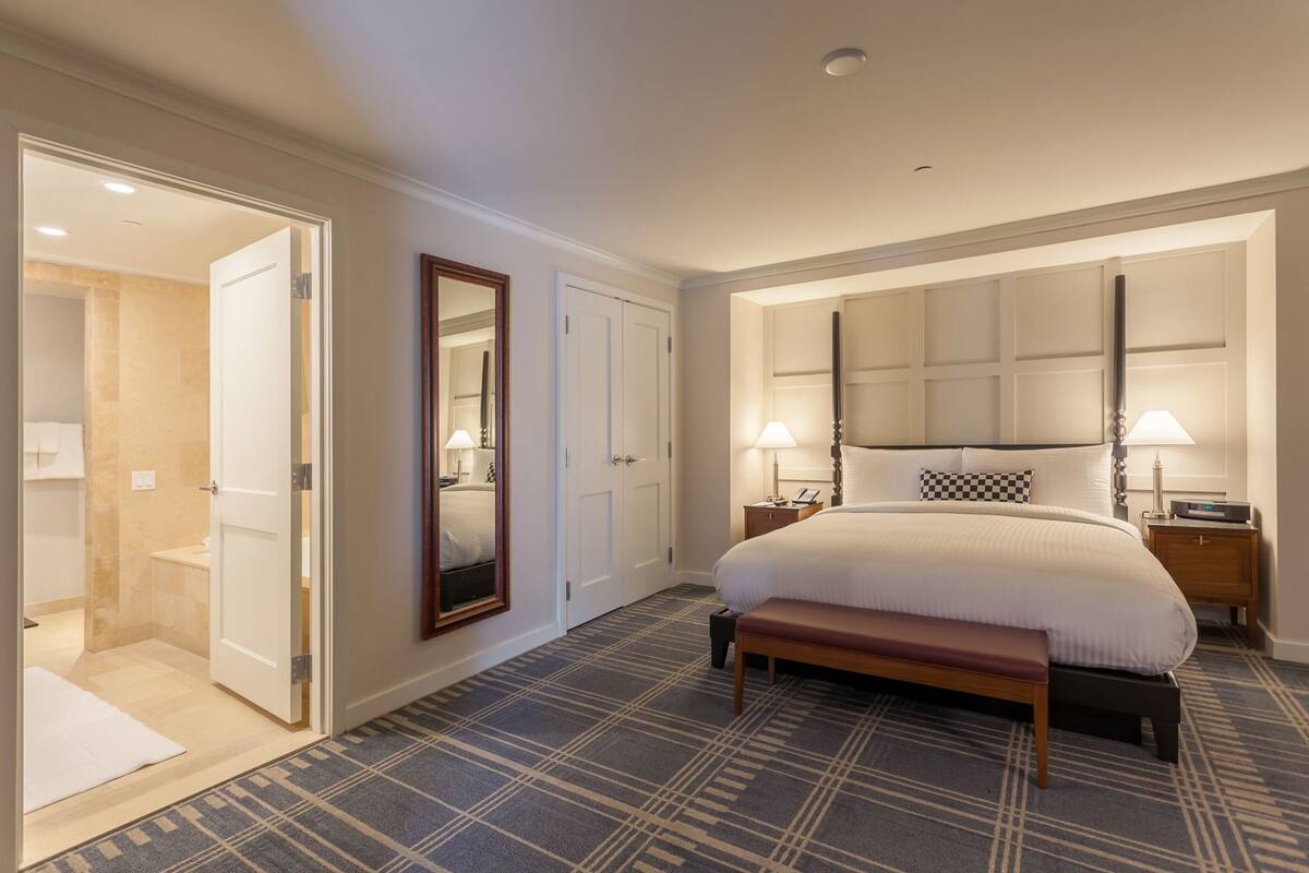 A hotel room with a large bed, bedside tables, a mirror, and a bench.