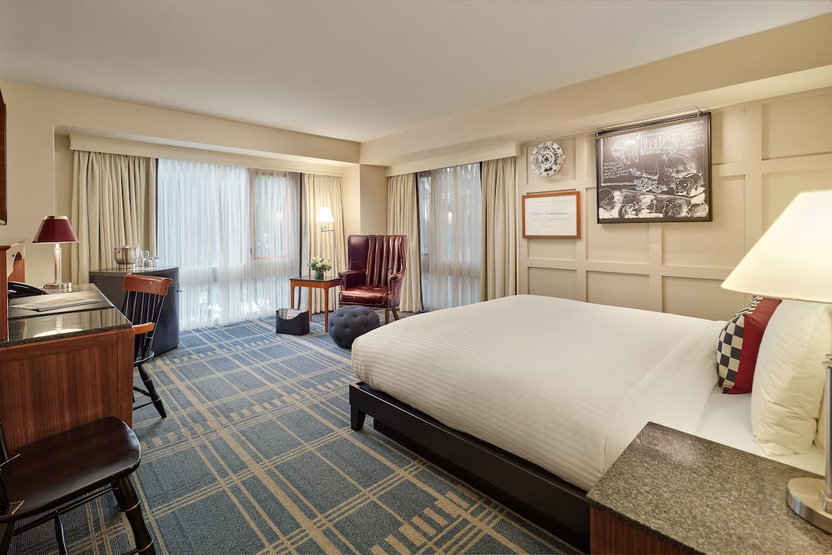 A hotel room with a large bed, a desk with a lamp, a chair, a small table, and a decorative plate on the wall.