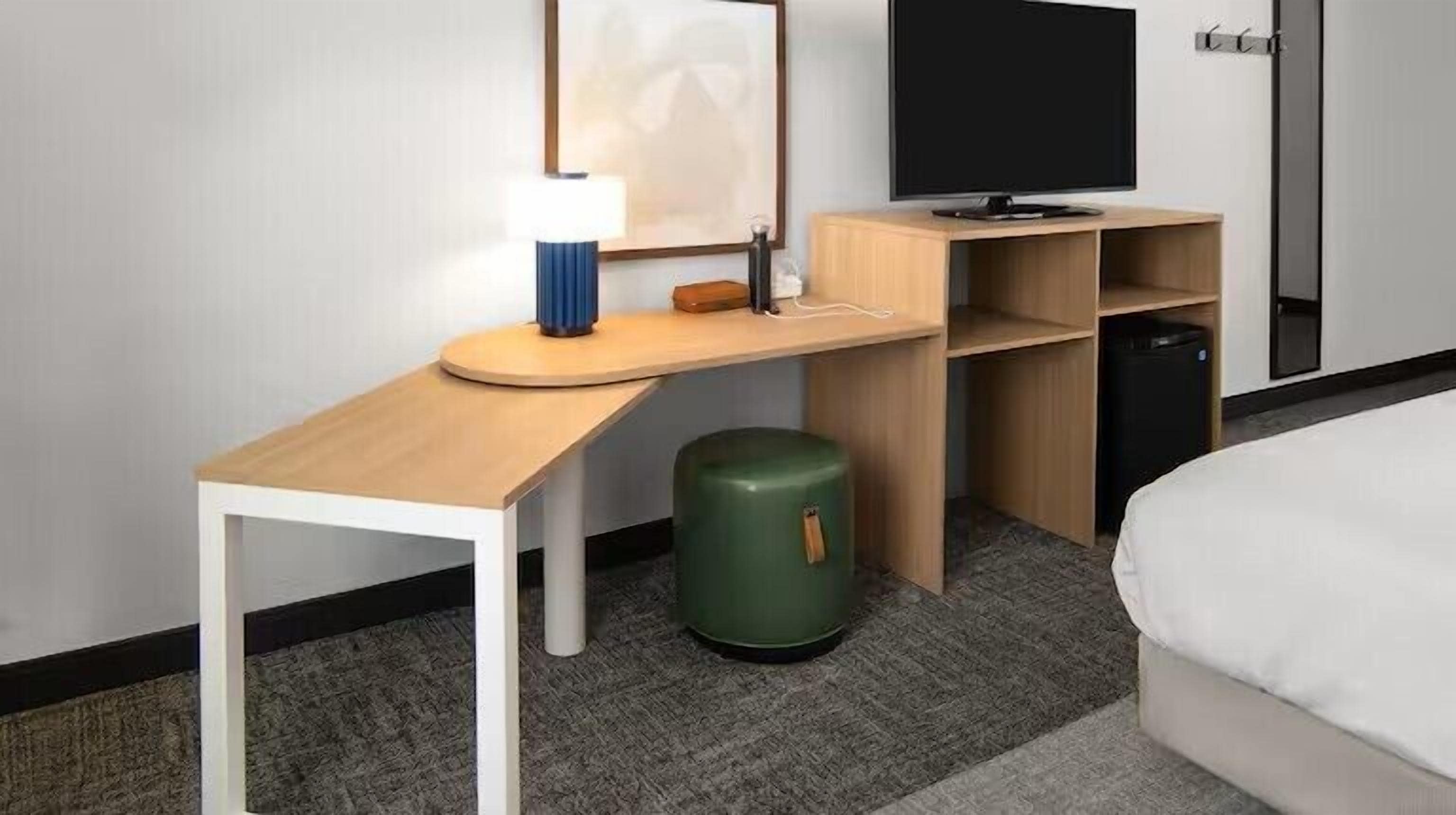 A hotel room with a bed, a desk with a lamp, a television, and a trash bin.