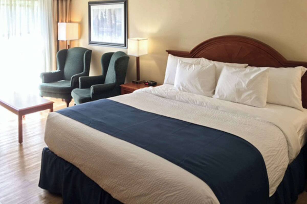 Ein Hotelzimmer mit einem großen Bett, zwei Stühlen, einem Nachttisch und einem gerahmten Bild an der Wand.