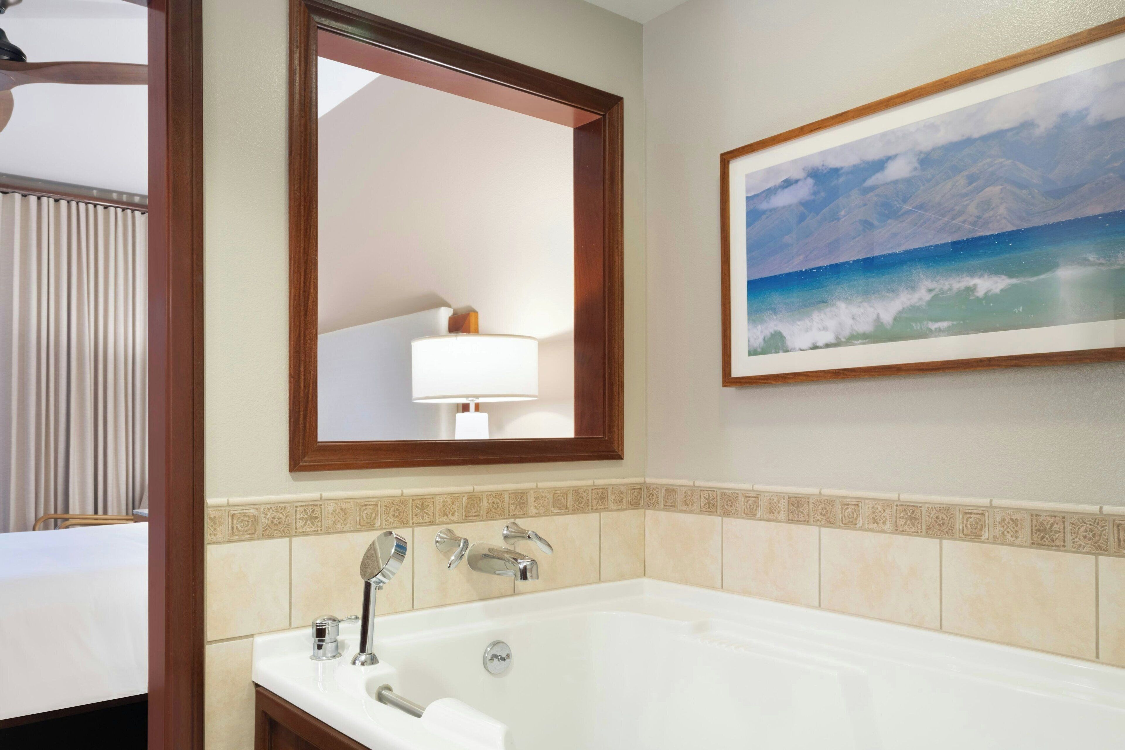 Une salle de bain d’hôtel avec une grande baignoire, un miroir et un tableau représentant une scène de plage.