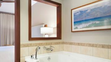 Une salle de bain d’hôtel avec une grande baignoire, un miroir et un tableau représentant une scène de plage.