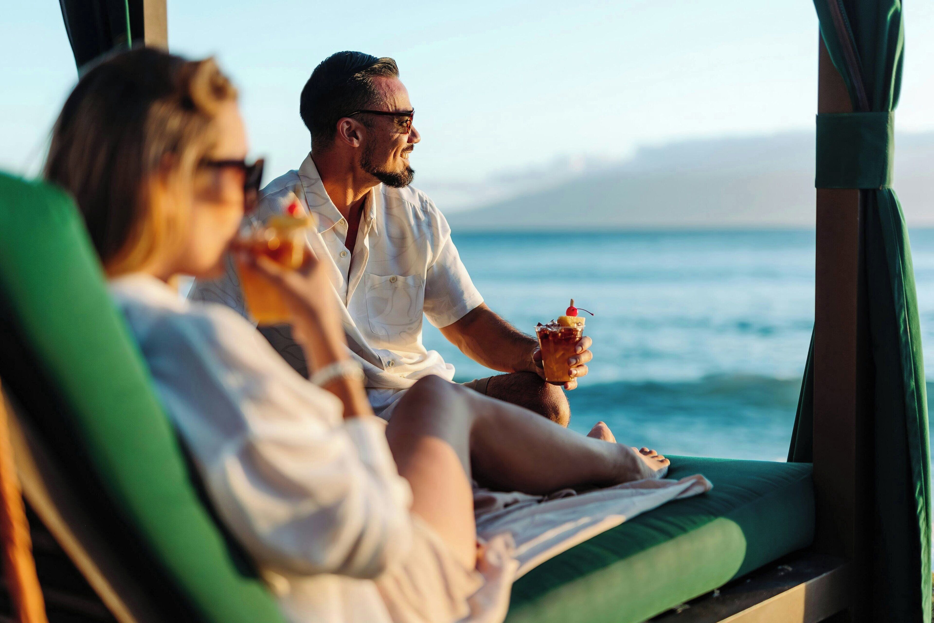 A couple relaxing on a sun lounger by a window with a view of the ocean.