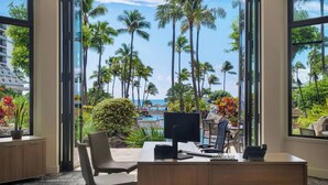 Un bureau moderne équipé d’un bureau, d’un ordinateur et d’une chaise, avec vue sur une piscine et des palmiers.