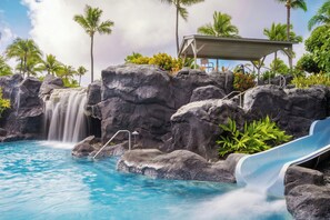 Una piscina con cascada, palmeras y un área de descanso cubierta.