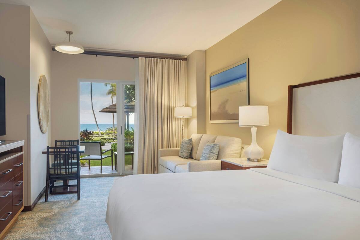 Une chambre d’hôtel comprenant un lit, un bureau avec une chaise, un canapé, une lampe et un tableau.
