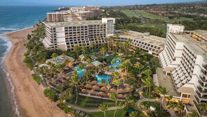 Een resort met meerdere gebouwen, een strand en een zwembad, omgeven door palmbomen.