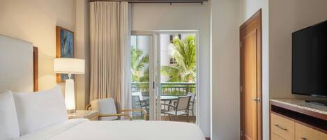A hotel room with a bed, a TV, a desk with a lamp, a chair, a balcony with a view of palm trees, and a sliding door.