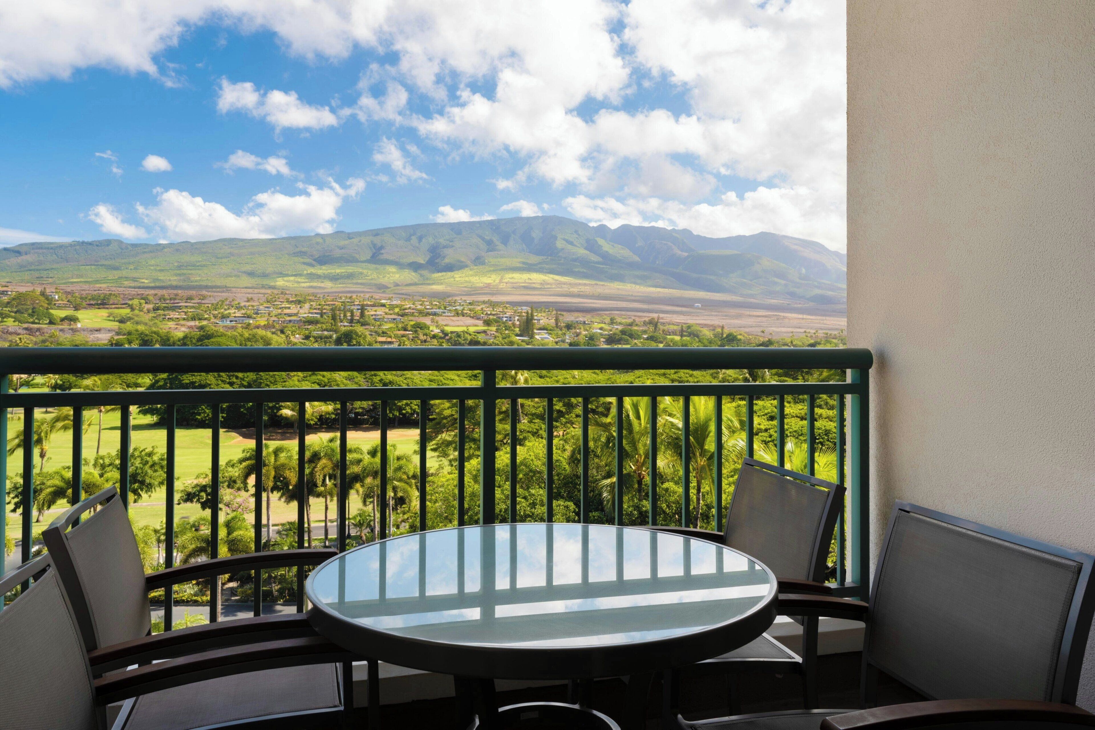 En balkong med ett runt bord och stolar, med utsikt över ett landskap med berg och grönskande natur.