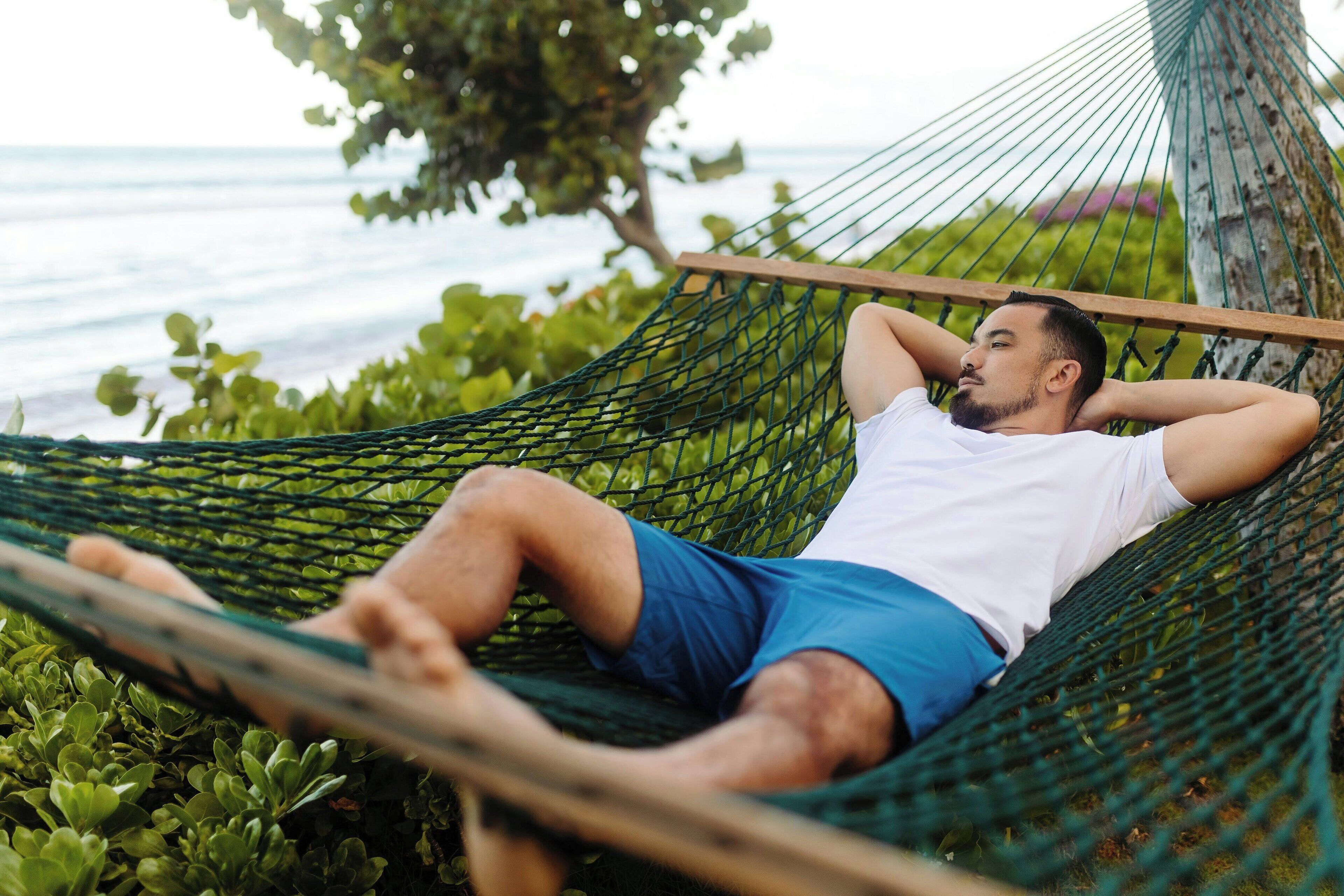Eine Person liegt in einer Hängematte im Freien mit Blick auf das Meer und viel Grün.