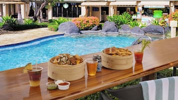 Un bar junto a la piscina con comida y bebidas, un letrero que indica un paseo por la playa y una tienda de alquileres.