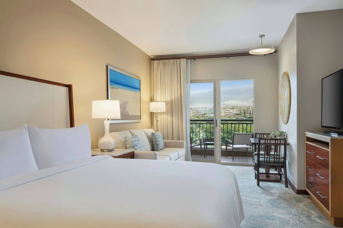 Une chambre d’hôtel avec un grand lit, un canapé, un bureau avec une chaise, une télévision et un balcon avec vue.