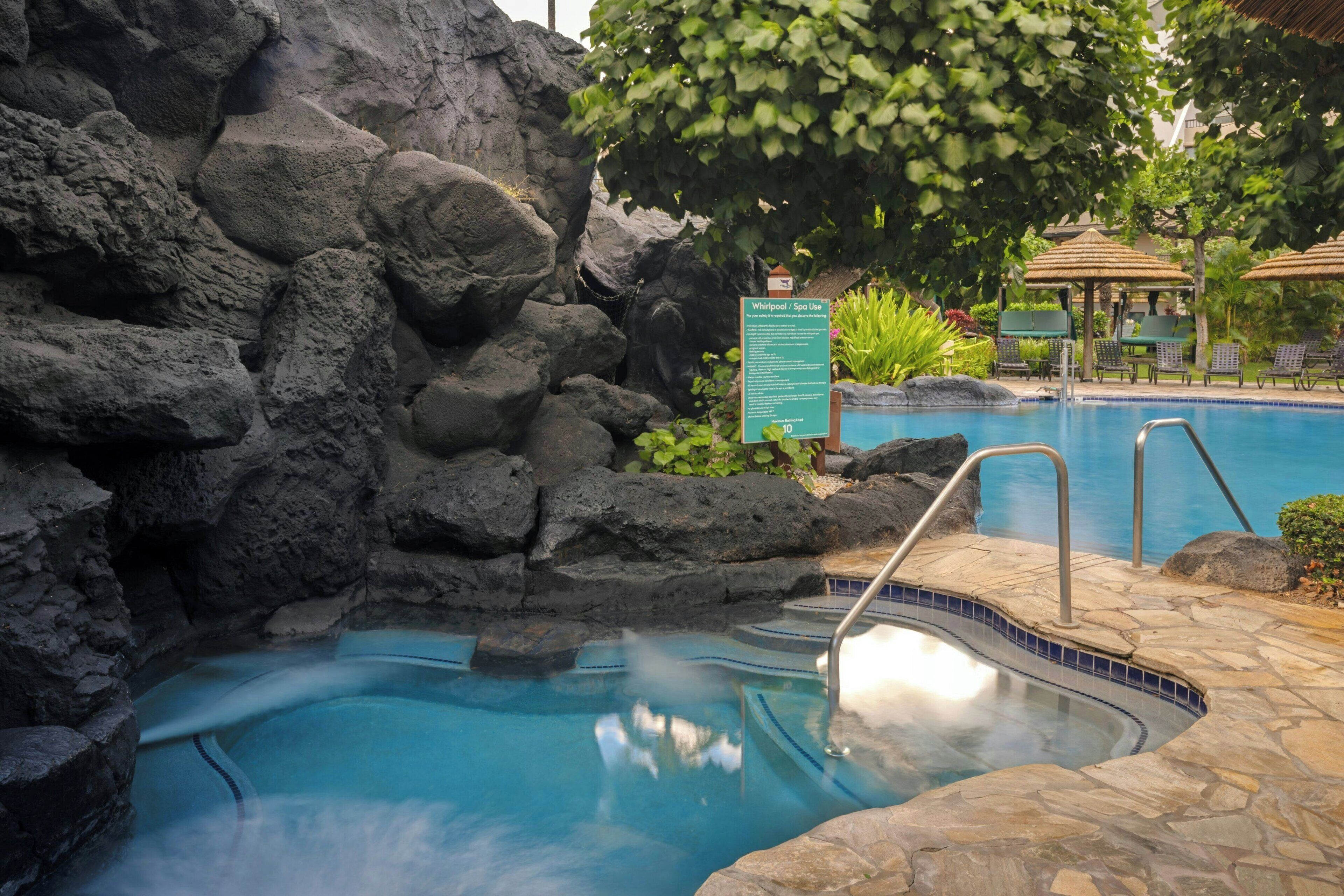 A pool with a rocky backdrop, a lounge area with umbrellas, and a sign indicating a spa.