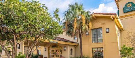 A hotel entrance with a palm tree, a brick pathway, and a sign reading "La Quinta Inn".
