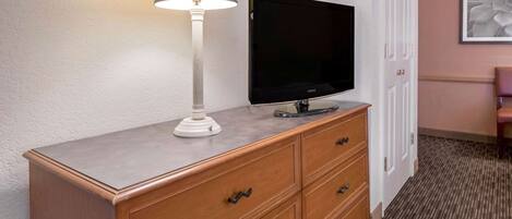 A wooden dresser with a flat-screen TV, a lamp, and a door with a framed picture.