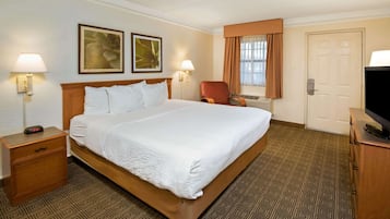 A hotel room with a large bed, two bedside lamps, a chair, a TV, and a door.