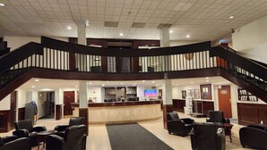 A hotel lobby with a reception desk, multiple seating areas, and a staircase connecting two floors. - Ramada by Wyndham London (London)