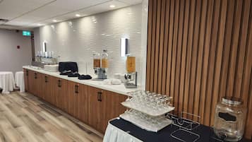 Disposição de buffet com dispensadores de comida, máquina de café e exposição de copos.