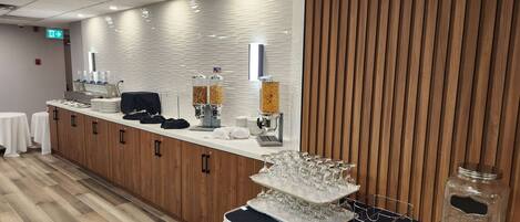 A buffet setup with food dispensers, a coffee machine, and a glassware display.