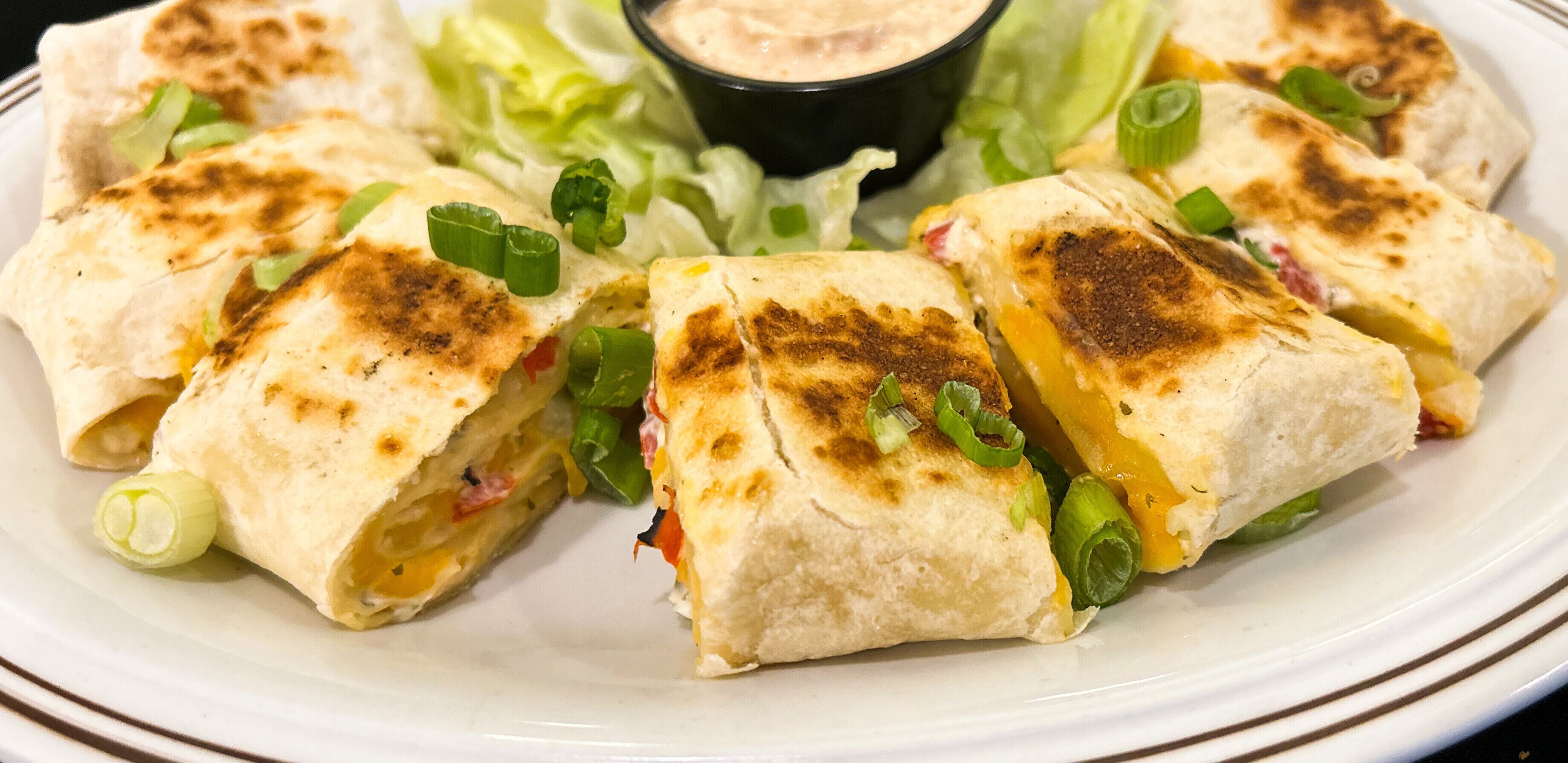 A plate of quesadillas with melted cheese, garnished with green onions, served with a side of lettuce and a dipping sauce.