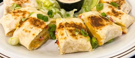 A plate of quesadillas with melted cheese, garnished with green onions, served with a side of lettuce and a dipping sauce.