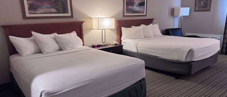 A hotel room with two beds, a desk, a chair, a lamp, and artwork on the walls.