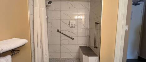A bathroom with a shower, a handrail, a towel rack, and a toilet.