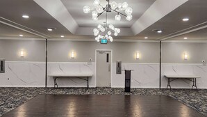 A spacious room with a dark wooden floor, marble walls, and a chandelier. There are two tables and a podium. - Ramada by Wyndham London (London)