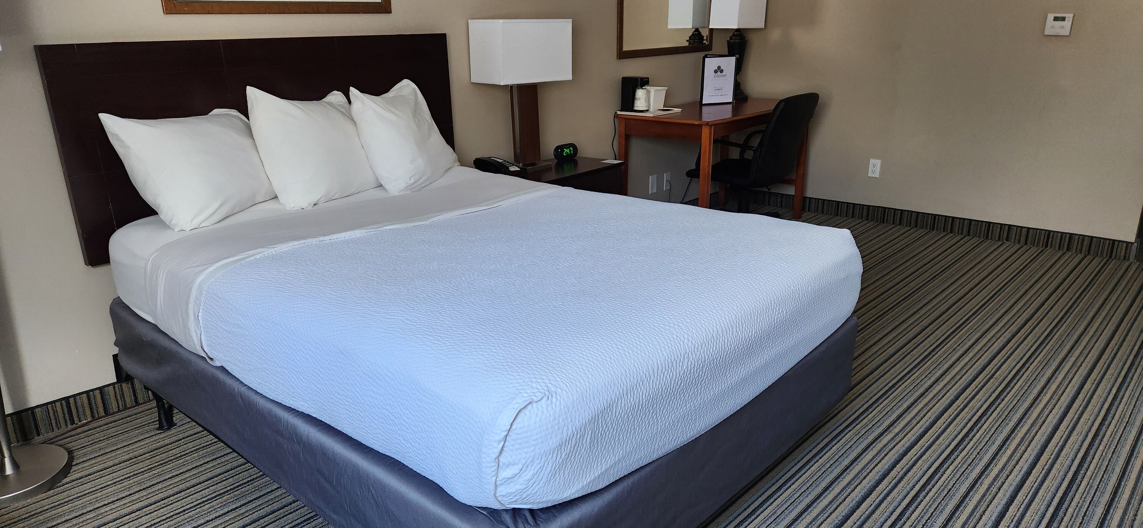 Una habitación de hotel con una cama grande, un escritorio, una silla, una lámpara y un reloj.