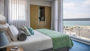 Een hotelkamer met een bed, nachtkastje, kledingkast en uitzicht op zee.