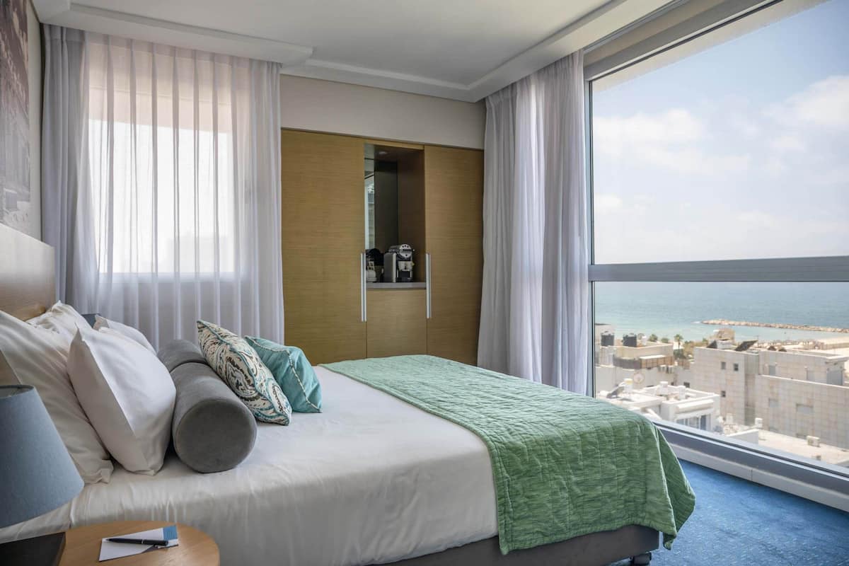 Ein Hotelzimmer mit Bett, Nachttisch, Kleiderschrank und Blick auf das Meer.