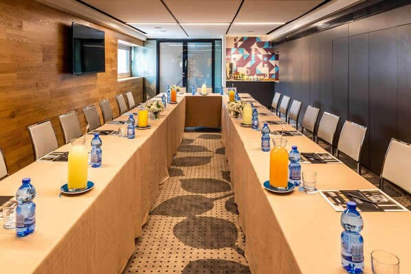 Un salón de conferencias con una larga mesa, sillas y botellas de agua.