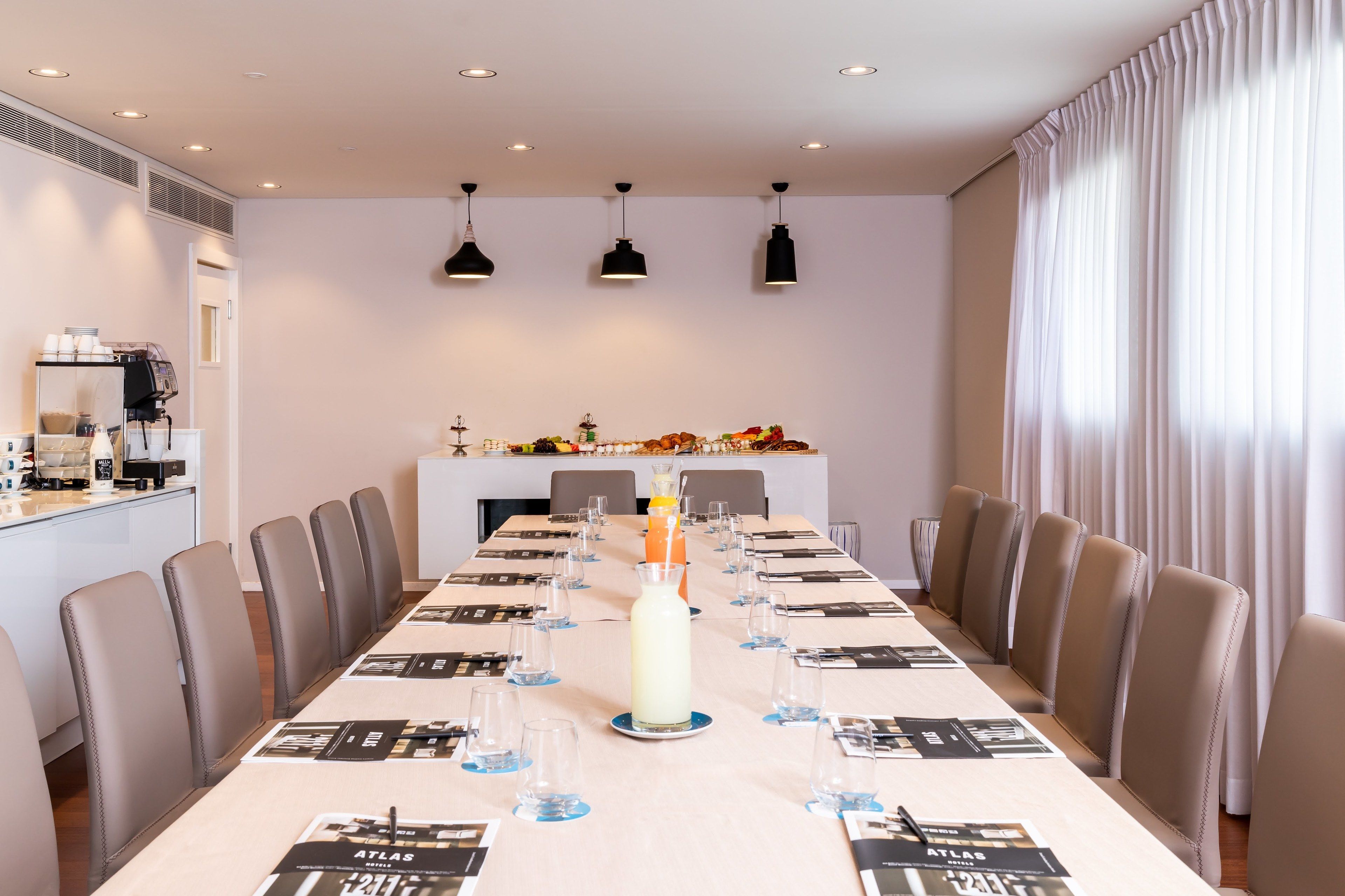 Un salón de conferencias con una larga mesa dispuesta para una reunión, equipado con sillas, una máquina de café y un centro de mesa decorativo.