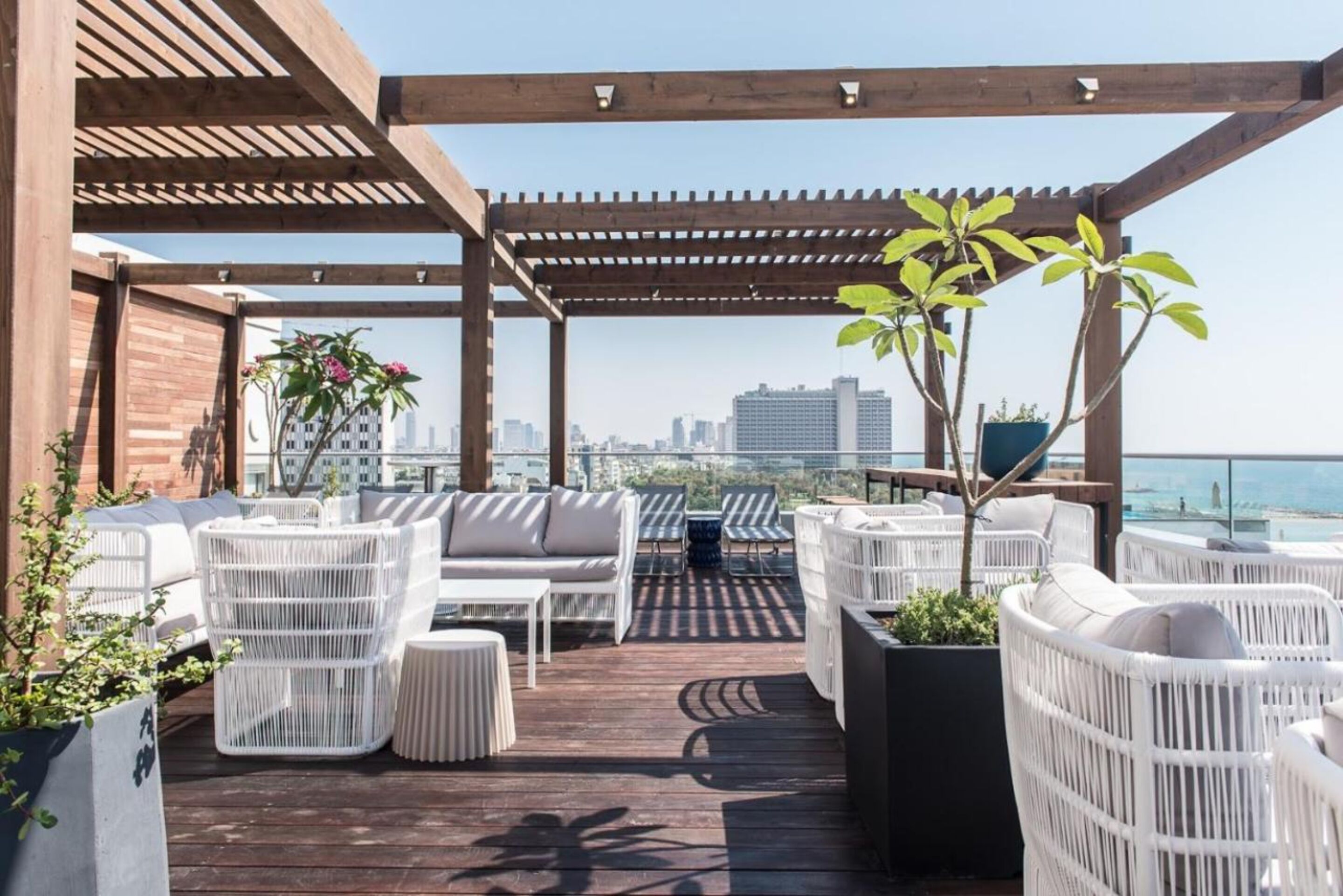 Un patio en la azotea con mobiliario de mimbre, plantas en macetas y vistas del horizonte de la ciudad.