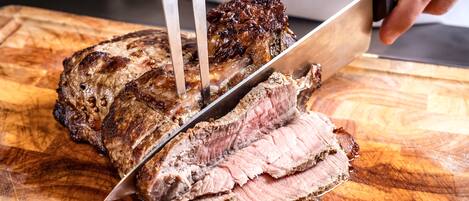 A person slicing a cooked steak on a wooden cutting board.
