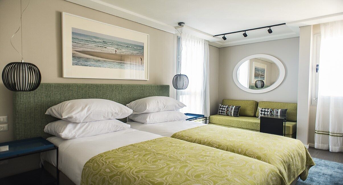 A hotel room with two beds, a desk, a chair, a mirror, and a framed picture on the wall.