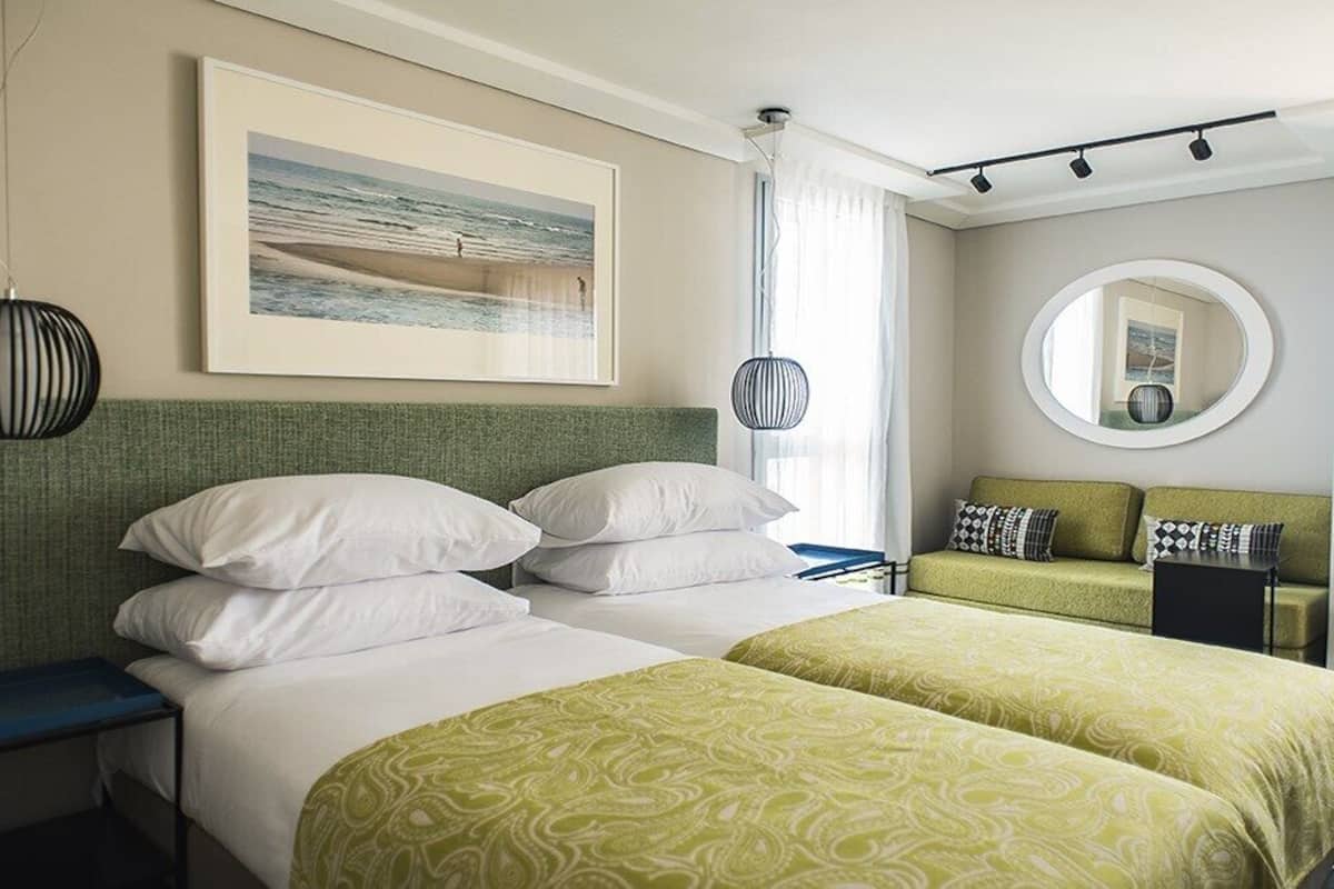 A hotel room with two beds, a desk, a chair, a mirror, and a framed picture on the wall.