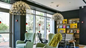 Een moderne lobby met twee lichtgroene fauteuils, een houten salontafel met boeken en een boekenkast in zwart en geel.