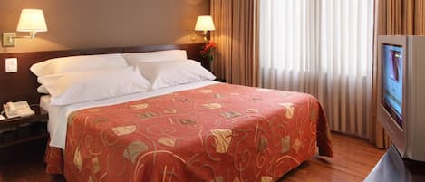 Habitación de hotel con una cama grande, dos lámparas de noche, un televisor y un teléfono en la mesita de noche.