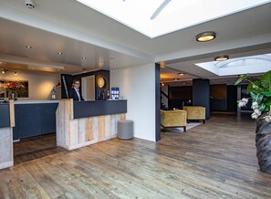 Un moderno vestíbulo de hotel con mostrador de recepción, un reloj y un área de descanso.