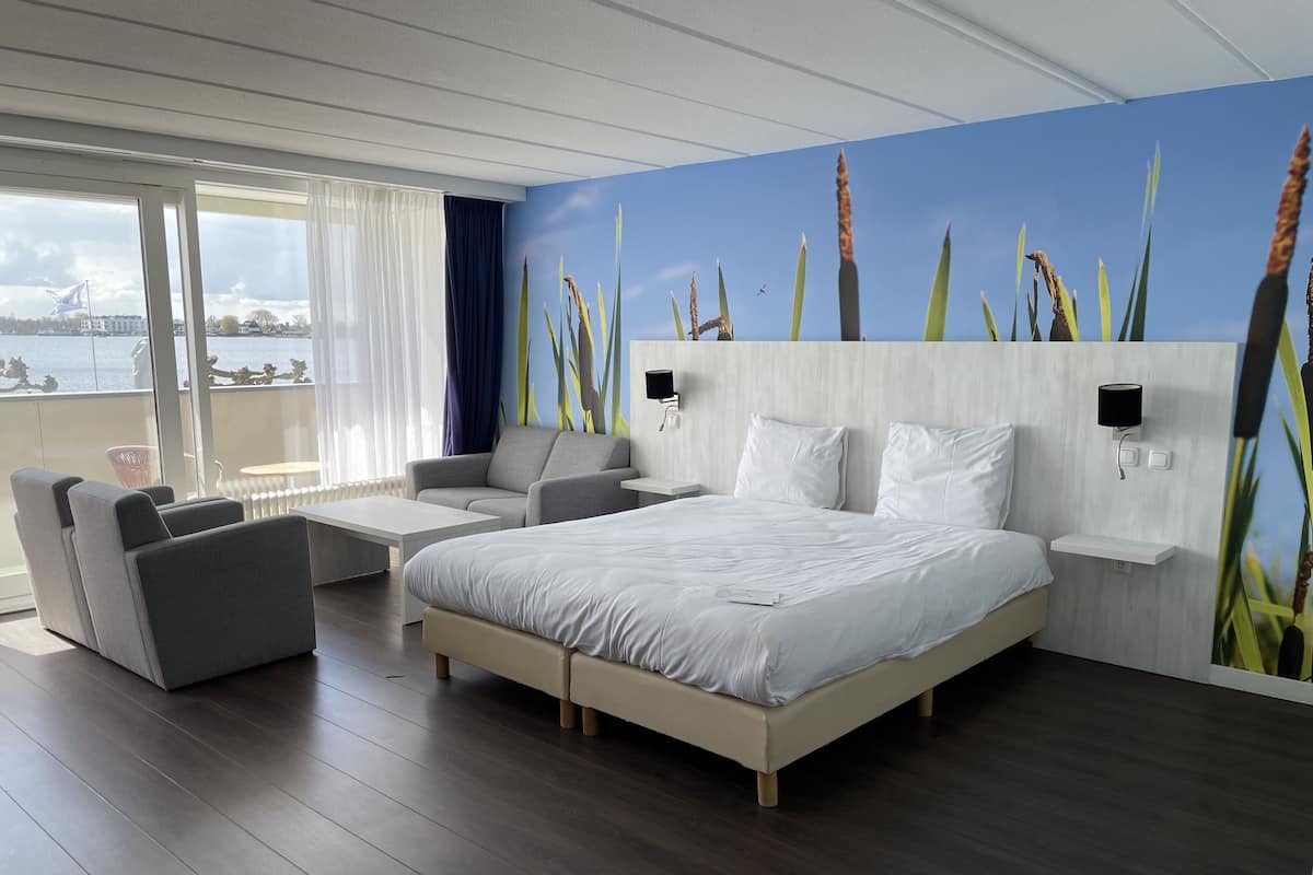 Une chambre d’hôtel moderne avec un grand lit, un canapé, une petite table et une vue sur la mer.
