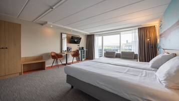 A hotel room with a bed, a desk, two chairs, a TV, and a large window.