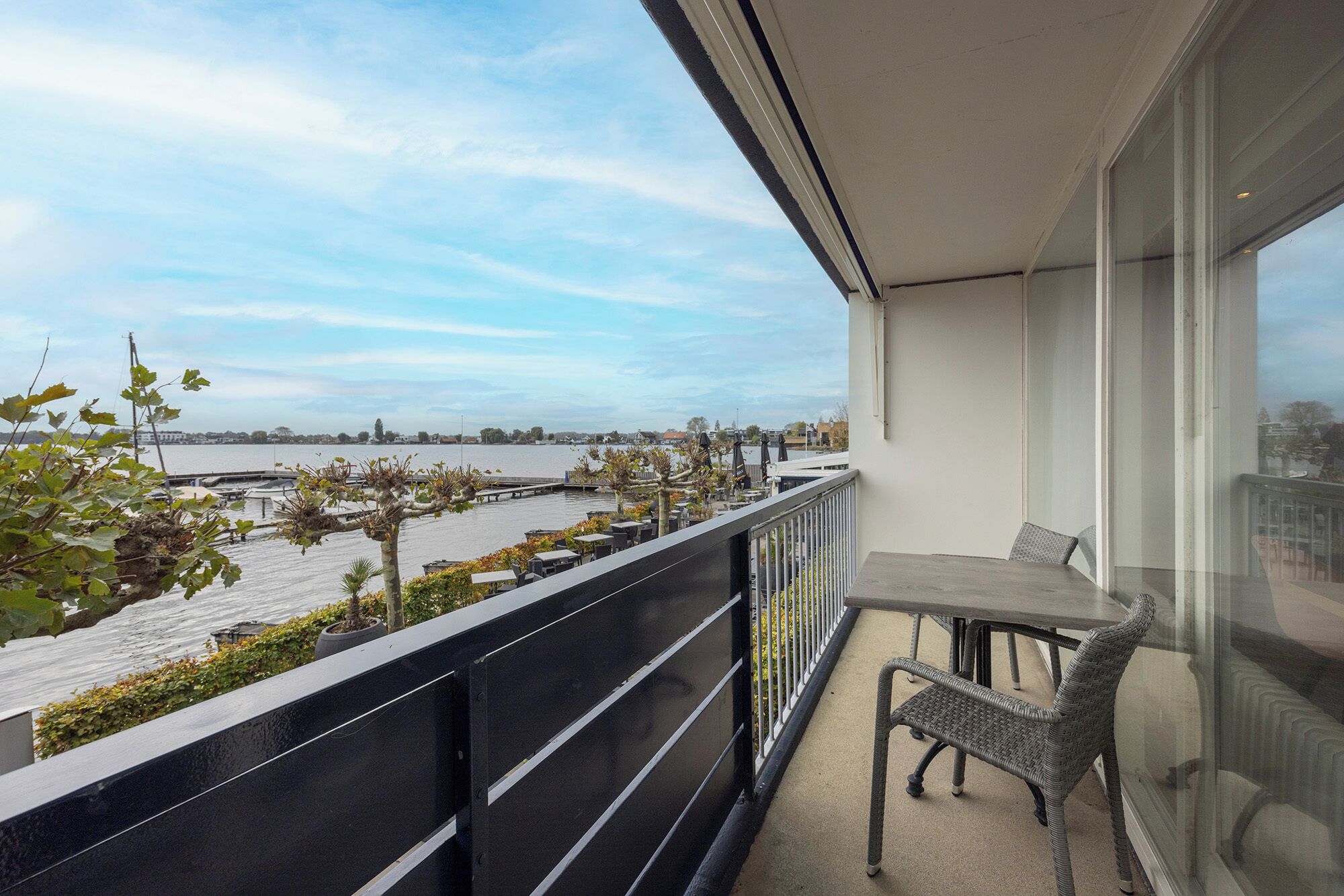 A balcony with a table and chair, overlooking a body of water and a distant shoreline.