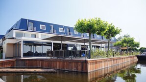 A waterfront property with a covered outdoor seating area, a wooden deck, and a reflection in the water. - Fletcher Hotel-Restaurant Loosdrecht - Amsterdam (Loosdrecht)