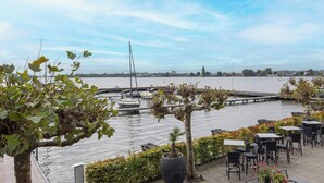 A waterfront patio with tables and chairs, a dock with boats, and a view of the water. - Fletcher Hotel-Restaurant Loosdrecht - Amsterdam (Loosdrecht)