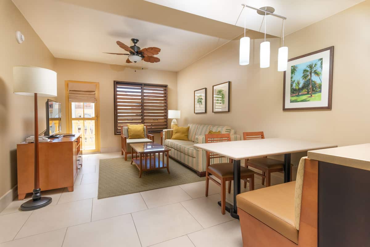 A well-lit living room with a sofa, dining table, and chairs. There is a ceiling fan, a lamp, and framed pictures on the wall.