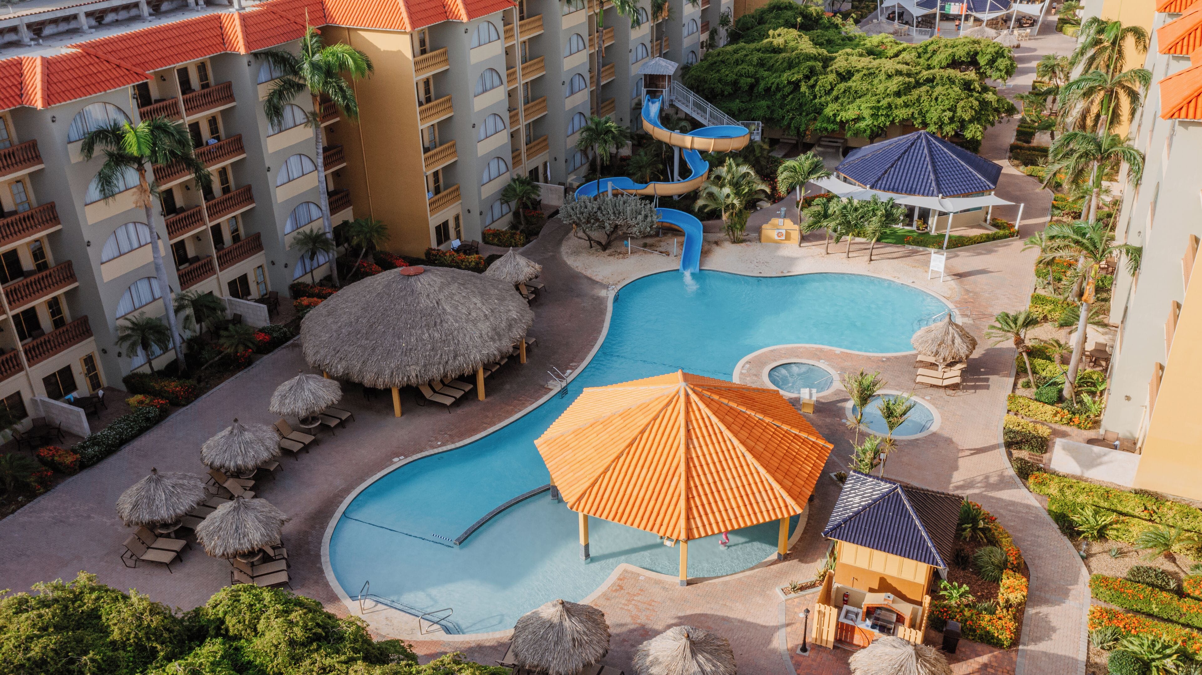 Un complejo turístico con múltiples piscinas, palmeras y sombrillas de paja.