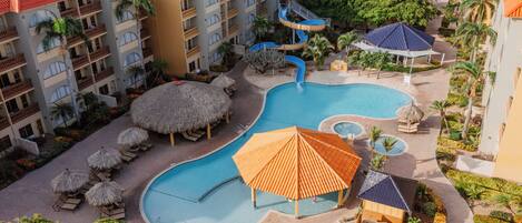 A resort with multiple swimming pools, palm trees, and thatched umbrellas.