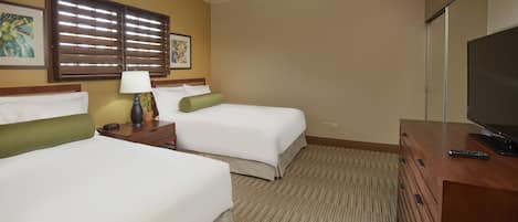 A hotel room with two beds, a desk with a lamp, a television, and artwork on the walls.